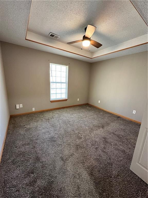 spare room with a ceiling fan, a tray ceiling, baseboards, and visible vents