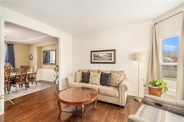 living room with a textured ceiling, dark wood-type flooring, a decorative wall, and wainscoting