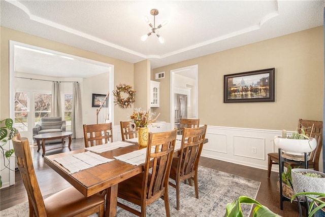 dining area with a tray ceiling, wood finished floors, visible vents, and wainscoting
