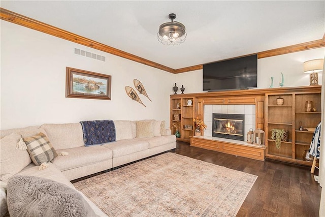 living room featuring dark wood-type flooring, a fireplace, visible vents, and ornamental molding