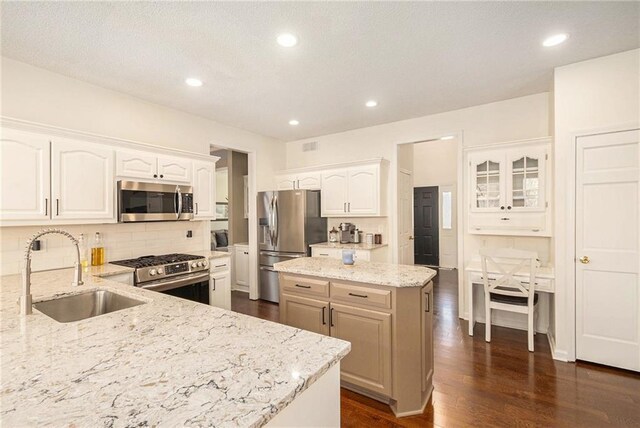 kitchen featuring backsplash, a center island, light stone countertops, stainless steel appliances, and a sink