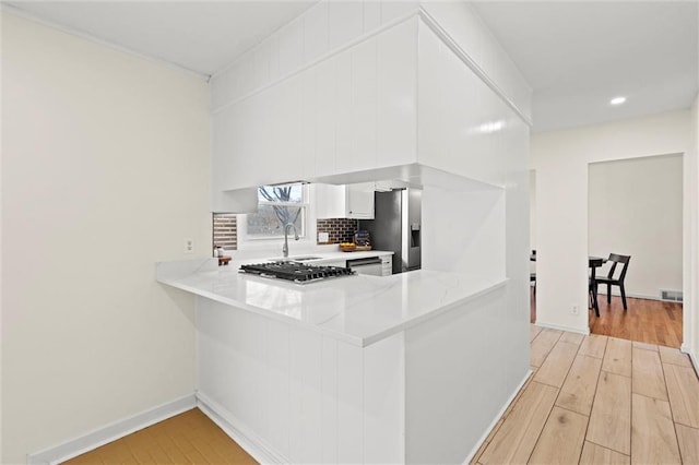 kitchen with light wood-style floors, a peninsula, stainless steel fridge with ice dispenser, light countertops, and decorative backsplash