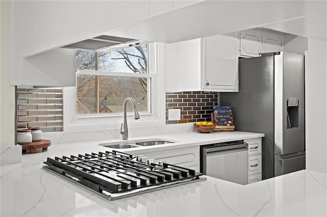 kitchen featuring light stone countertops, decorative backsplash, appliances with stainless steel finishes, white cabinetry, and a sink