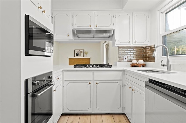 kitchen with a sink, light countertops, under cabinet range hood, and stainless steel appliances