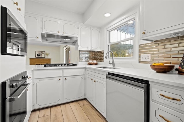 kitchen with light wood-style flooring, a sink, stainless steel appliances, under cabinet range hood, and white cabinetry