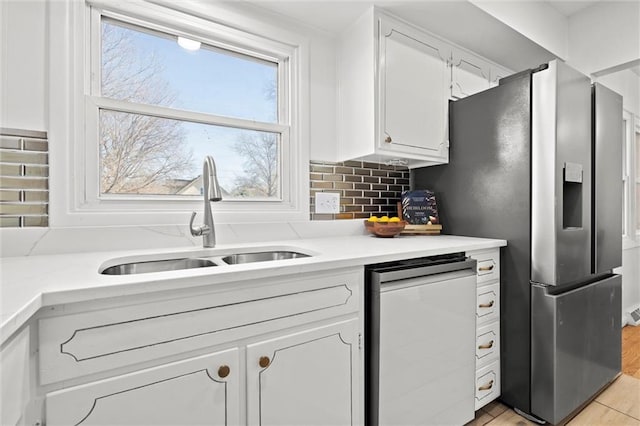 kitchen with tasteful backsplash, stainless steel fridge with ice dispenser, light countertops, white cabinetry, and a sink