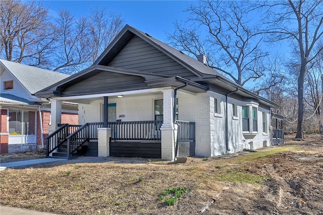 bungalow featuring a porch, brick siding, and a chimney