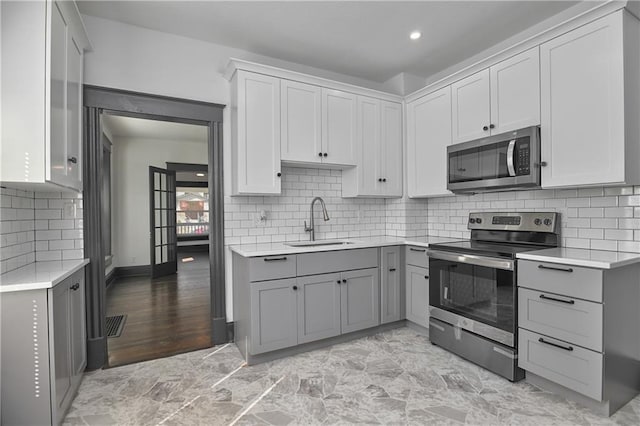 kitchen with gray cabinetry, a sink, tasteful backsplash, appliances with stainless steel finishes, and light countertops