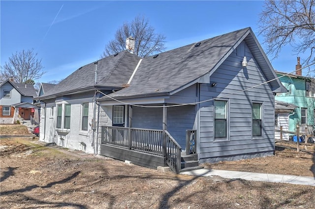 back of property with a porch, brick siding, and a chimney