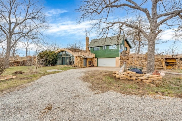 view of front facade featuring a garage, gravel driveway, and a chimney