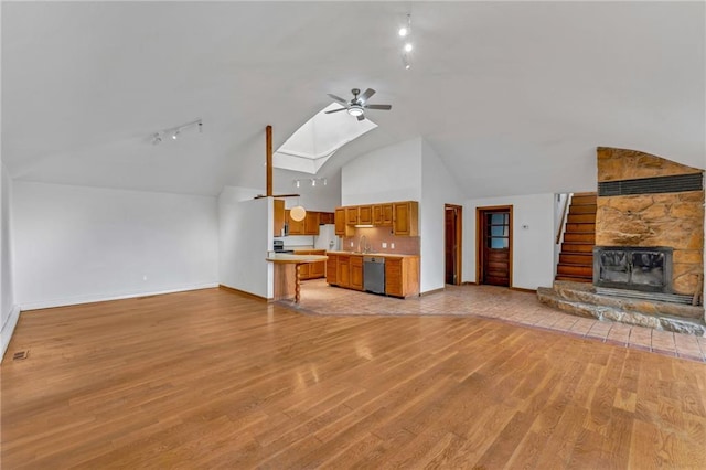 unfurnished living room with baseboards, a stone fireplace, light wood-style flooring, a skylight, and a ceiling fan