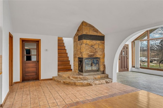 unfurnished living room featuring wood finished floors, arched walkways, a fireplace, lofted ceiling, and stairs