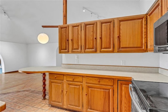 kitchen featuring brown cabinets, track lighting, stainless steel microwave, light countertops, and light tile patterned floors