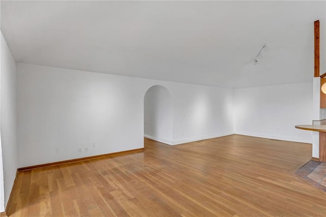 additional living space with wood finished floors, arched walkways, and baseboards