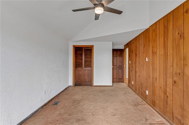 unfurnished bedroom featuring visible vents, a closet, wooden walls, light colored carpet, and ceiling fan