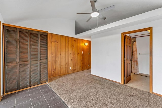 unfurnished bedroom featuring lofted ceiling, carpet, wooden walls, tile patterned flooring, and baseboards