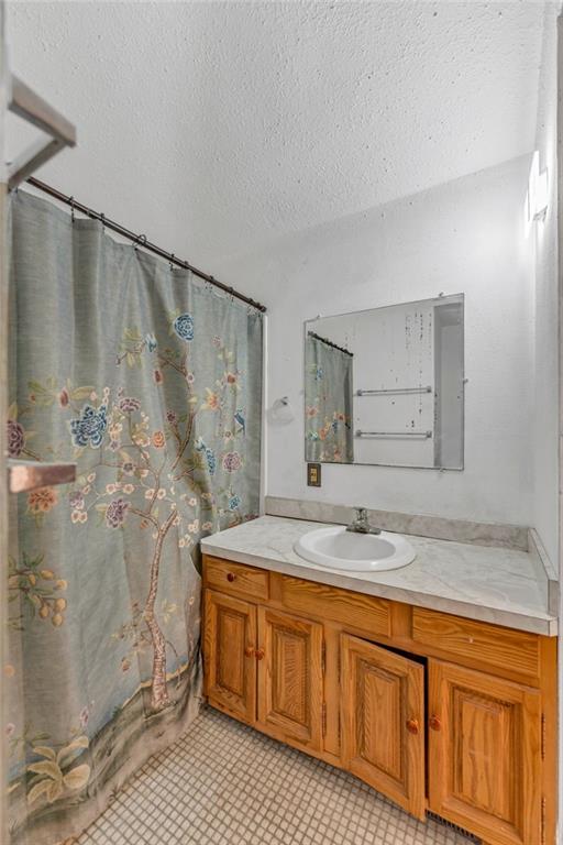 full bath with vanity, curtained shower, and a textured ceiling