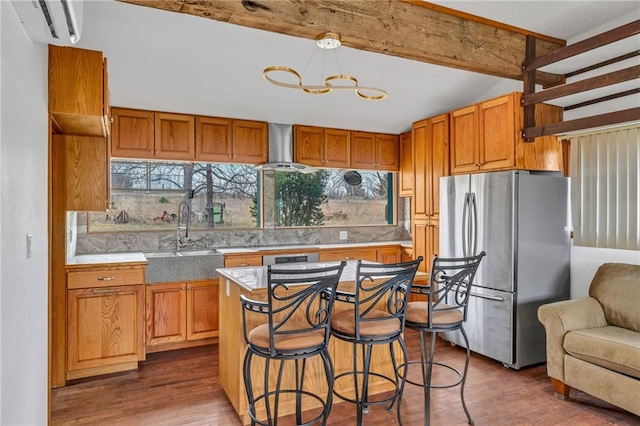 kitchen with dark wood finished floors, freestanding refrigerator, a sink, an AC wall unit, and wall chimney exhaust hood