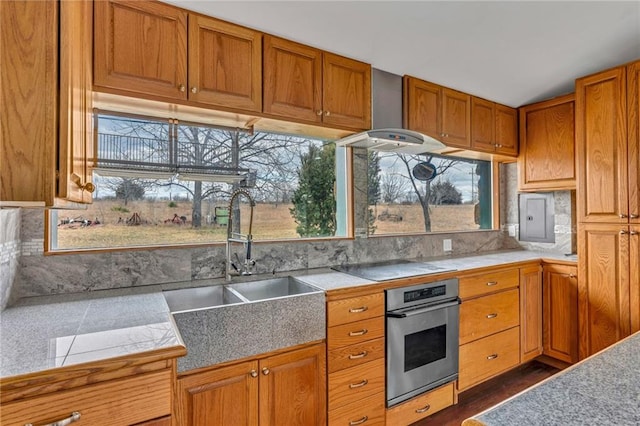 kitchen with brown cabinetry, electric panel, a sink, oven, and electric stovetop