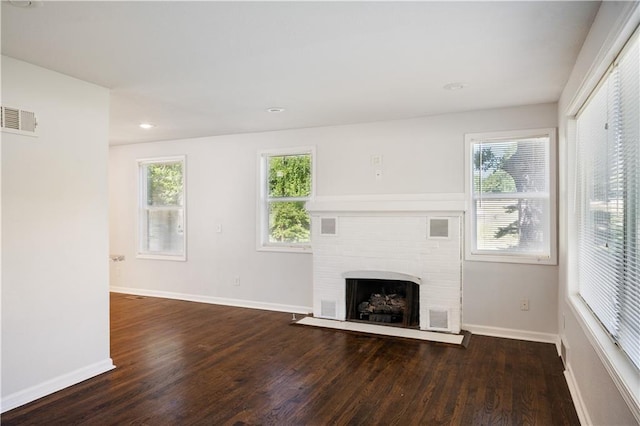 unfurnished living room with a wealth of natural light, visible vents, a fireplace, and wood finished floors