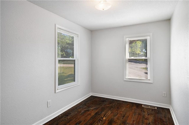 empty room with visible vents, dark wood-type flooring, and baseboards