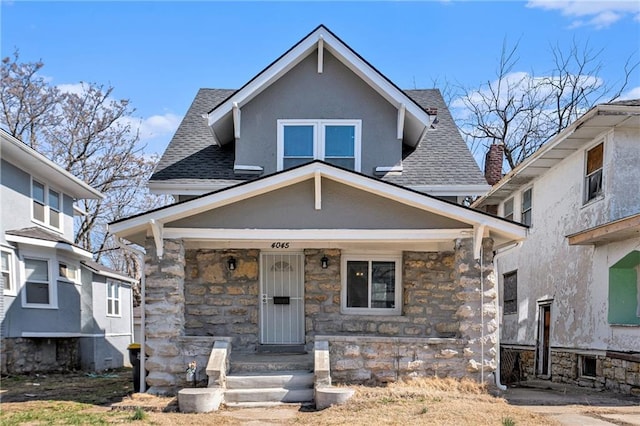 view of front of home with stone siding, covered porch, roof with shingles, and stucco siding