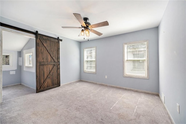 unfurnished bedroom featuring light carpet, baseboards, and a barn door