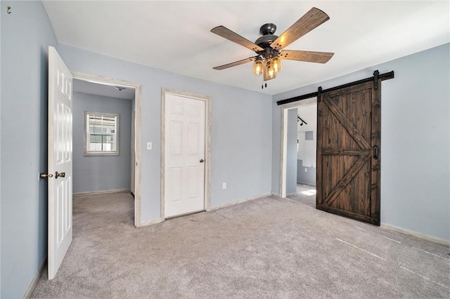 unfurnished bedroom with connected bathroom, ceiling fan, baseboards, a barn door, and carpet flooring