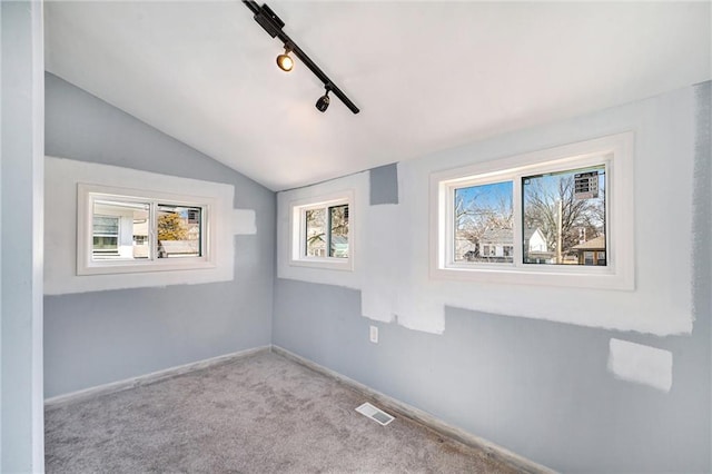 carpeted empty room with visible vents, rail lighting, baseboards, and vaulted ceiling