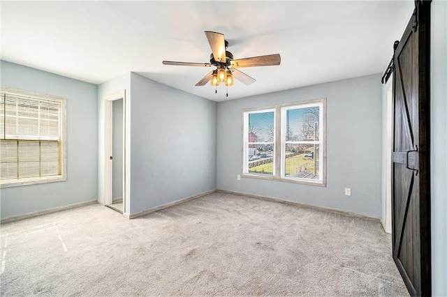 unfurnished bedroom with light carpet, baseboards, and a barn door