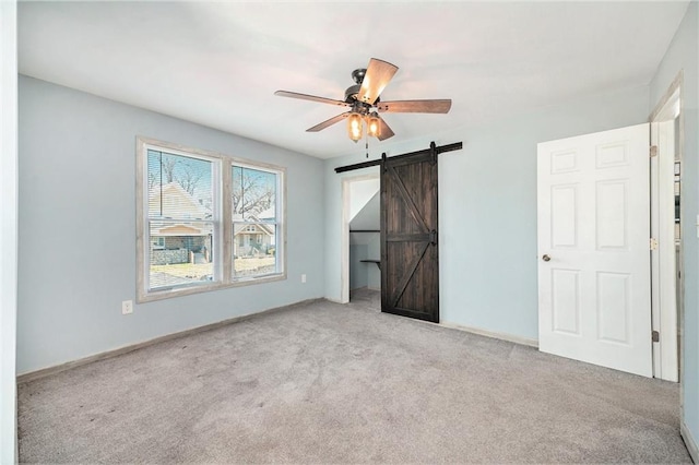 unfurnished bedroom featuring a barn door, carpet floors, baseboards, and a ceiling fan