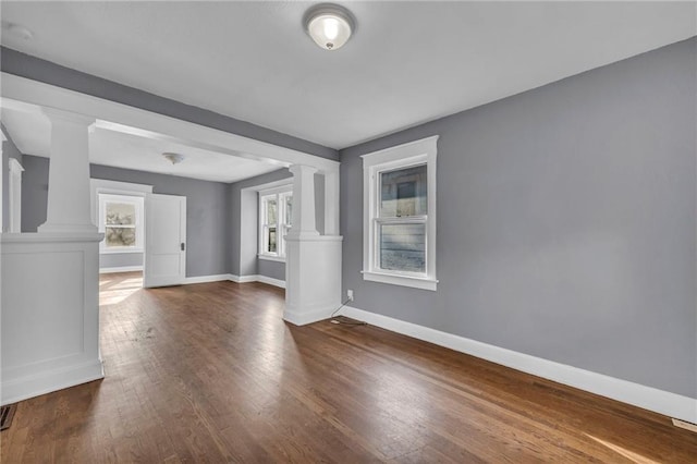 unfurnished room featuring dark wood-style floors, visible vents, baseboards, and decorative columns