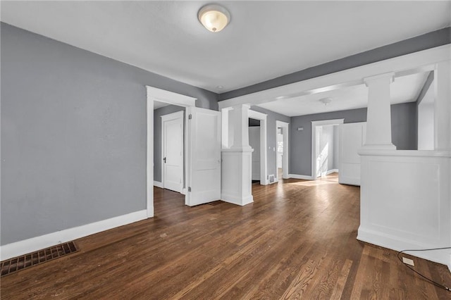 unfurnished room featuring visible vents, baseboards, dark wood-style flooring, and ornate columns