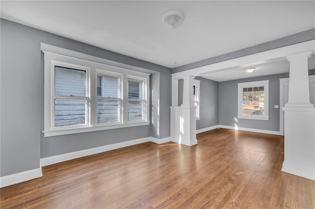 unfurnished room featuring baseboards, wood finished floors, and ornate columns