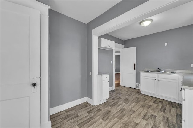 interior space featuring light wood-style flooring, white cabinets, baseboards, and a sink