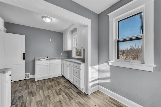 kitchen featuring wood finished floors, white cabinetry, baseboards, and a sink