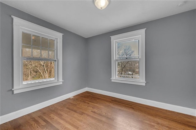 unfurnished room featuring wood finished floors, a healthy amount of sunlight, and baseboards