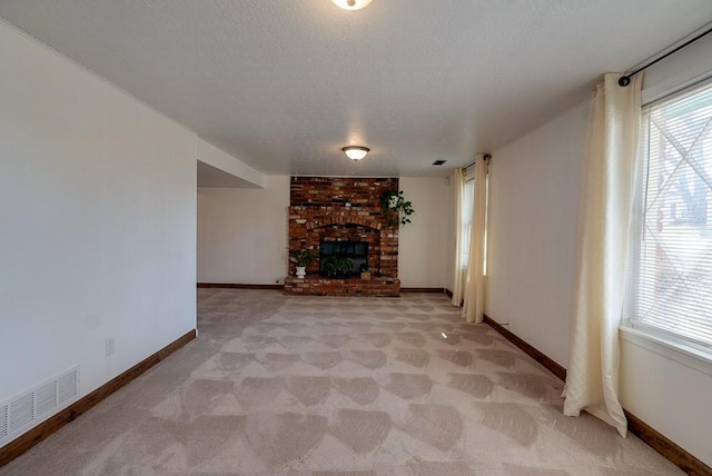 unfurnished living room featuring baseboards, visible vents, a textured ceiling, a brick fireplace, and light colored carpet