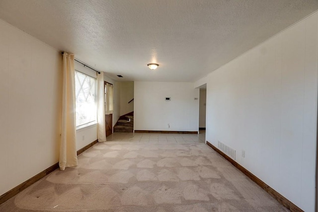 unfurnished room featuring visible vents, light colored carpet, stairs, and a textured ceiling