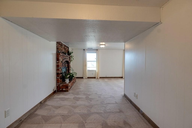 hall featuring baseboards, light carpet, and a textured ceiling