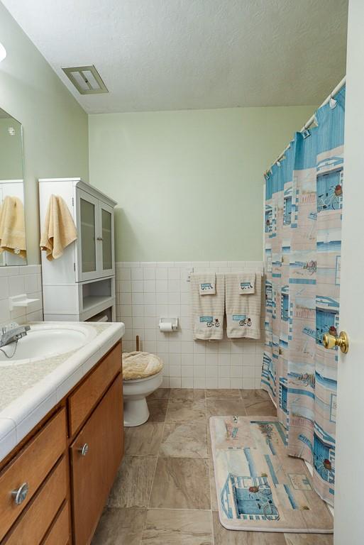 bathroom with visible vents, a wainscoted wall, toilet, tile walls, and vanity