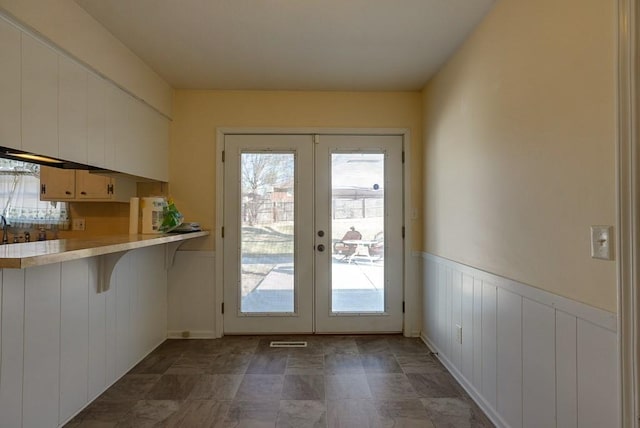 doorway to outside featuring a wainscoted wall, plenty of natural light, visible vents, and french doors