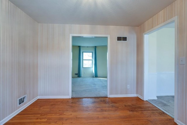 unfurnished room featuring baseboards, wood finished floors, visible vents, and a textured ceiling