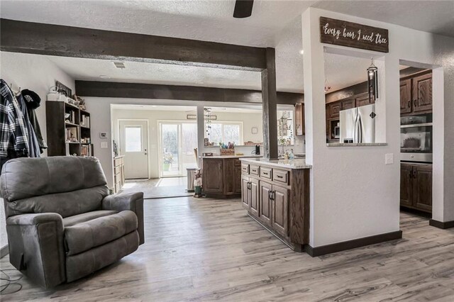 living area with light wood-style flooring, beamed ceiling, and a textured ceiling