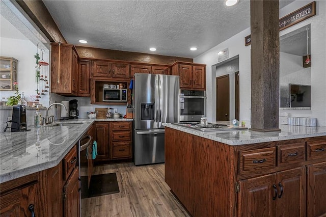 kitchen with light wood-type flooring, light stone counters, appliances with stainless steel finishes, a textured ceiling, and a sink