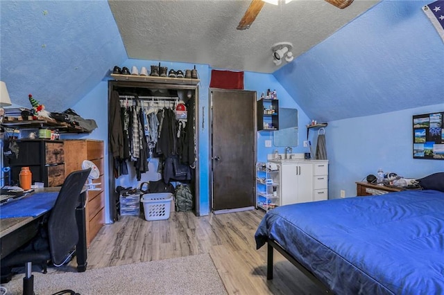 bedroom with lofted ceiling, wood finished floors, a closet, a textured ceiling, and a ceiling fan