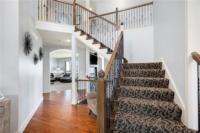 staircase featuring wood finished floors, arched walkways, a towering ceiling, and baseboards