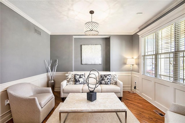 living room with visible vents, wood finished floors, and ornamental molding