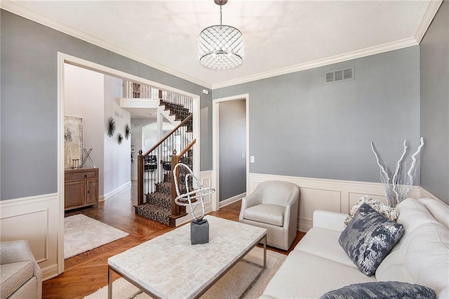 living room with visible vents, crown molding, a chandelier, stairway, and wainscoting