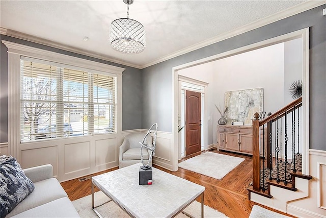 living area with a wainscoted wall, wood finished floors, stairway, an inviting chandelier, and crown molding